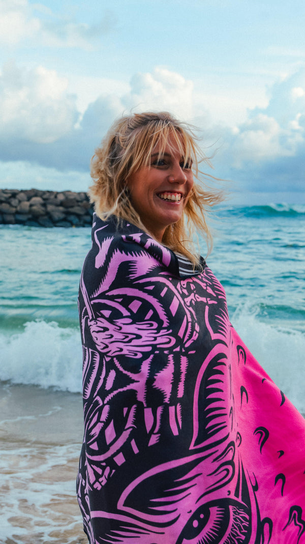 A woman smiling on a beach wrapped in a Happy Faced Towel