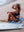 A woman sits on a Happy Faced Towel at the beach