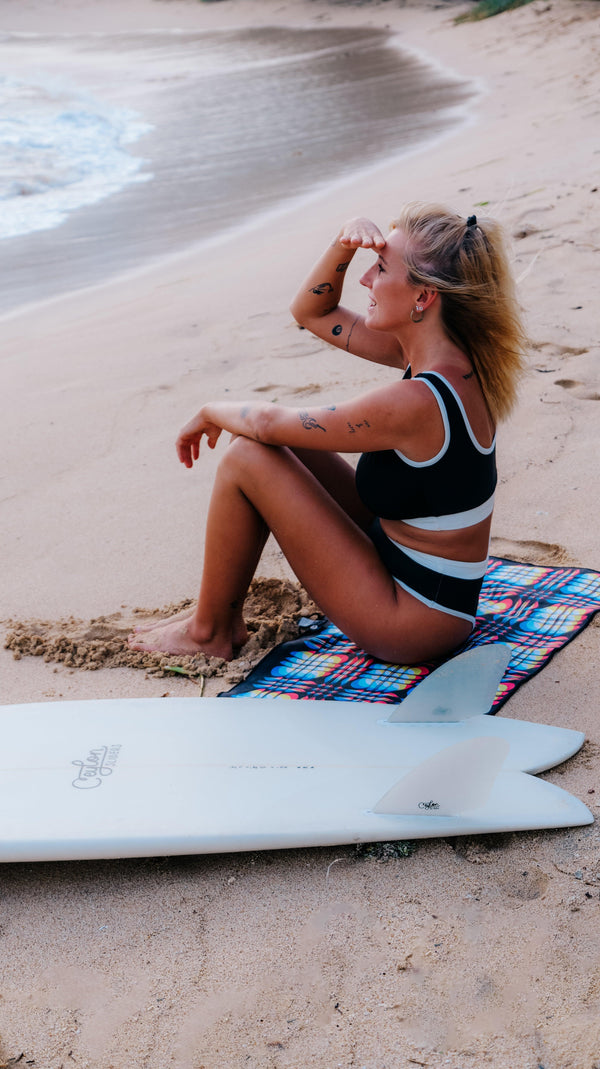 A woman sits on a Happy Faced Towel at the beach