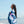 A woman wrapped in a colorful blue towel stands on the beach, gazing peacefully toward the horizon with a slight smile on her face. The towel features a bold, abstract design with pink and white elements. The ocean waves gently roll onto the shore behind her, and the sky is clear and bright, enhancing the serene and relaxed beach atmosphere. Her long dark hair flows slightly in the breeze, adding to the calm and carefree mood of the scene.
