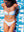 A woman in a white bikini is lying on a colorful beach towel with an abstract design and bold white text. She is smiling and looking down, with her hands resting by her sides on the towel. The bright sunlight highlights her tan skin, and the vibrant towel creates a playful and summery atmosphere. The image is a close-up, capturing her upper body and part of the towel beneath her.