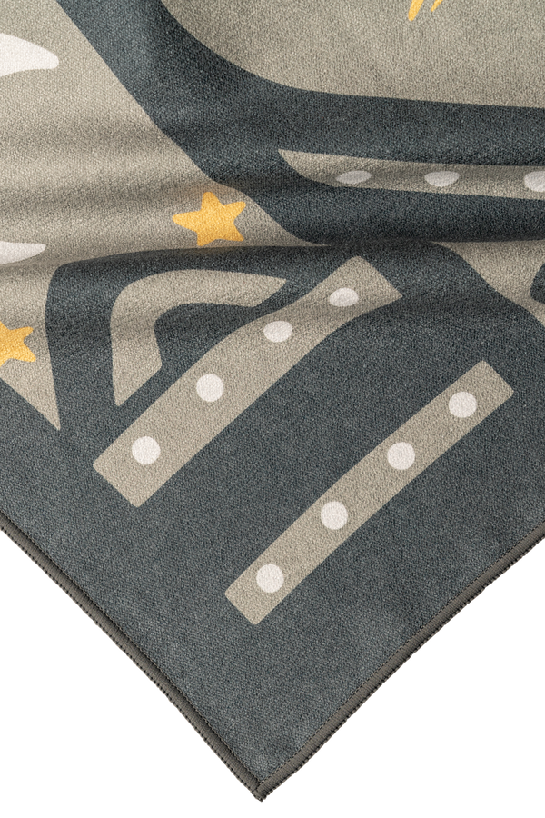 A close-up of a folded corner of a towel featuring a celestial design. The visible part of the towel shows dark gray and light gray geometric shapes with white dotted lines and small yellow stars. The fabric has a smooth texture, and the edges are neatly stitched in dark gray, showcasing quality craftsmanship. The detailed pattern adds a playful cosmic touch, blending modern and celestial elements.