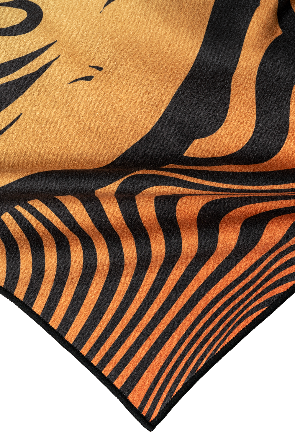A close-up of a towel corner showcasing an abstract tiger stripe pattern in vibrant orange and black. The design features flowing, wavy lines that create a dynamic, hypnotic effect, blending smoothly into the fabric. The color transitions from deep orange to lighter shades, with bold black stripes adding contrast. The texture of the towel appears soft and plush, emphasizing both the artistic detail and quality of the material.