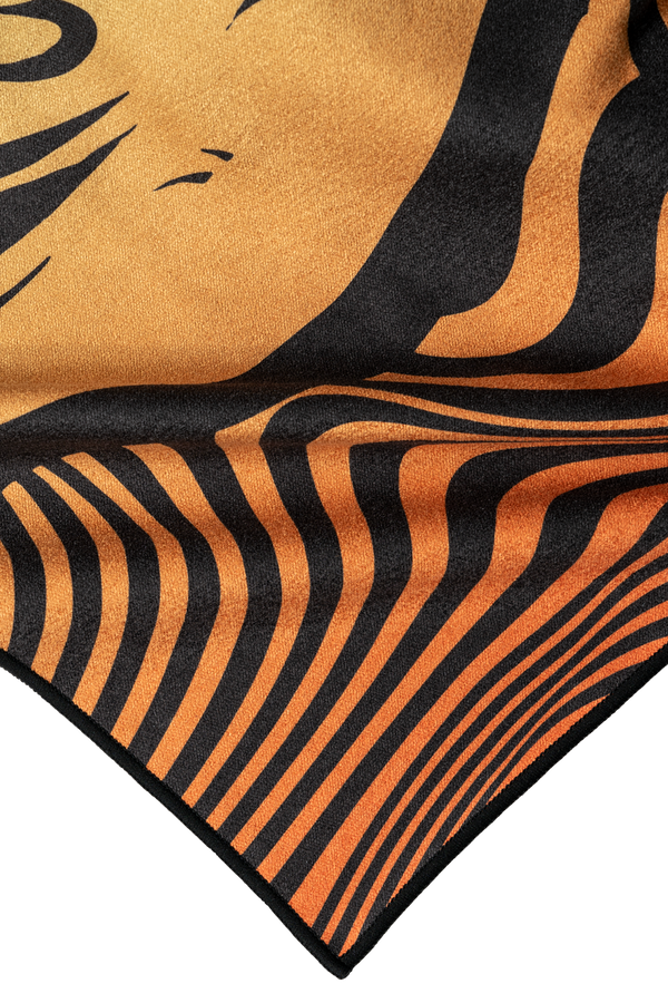 A close-up of a towel corner showcasing an abstract tiger stripe pattern in vibrant orange and black. The design features flowing, wavy lines that create a dynamic, hypnotic effect, blending smoothly into the fabric. The color transitions from deep orange to lighter shades, with bold black stripes adding contrast. The texture of the towel appears soft and plush, emphasizing both the artistic detail and quality of the material.