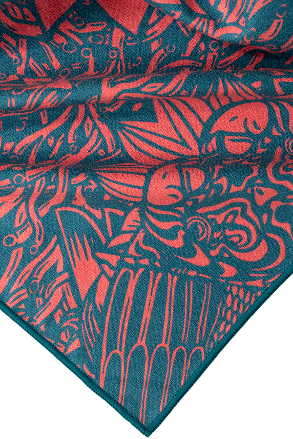 A close-up view of a towel corner featuring a vibrant abstract design in coral and teal. The intricate pattern includes various shapes and lines, creating a dynamic, artistic look with bold, organic elements. The coral designs stand out against the deep teal background, giving the towel a lively, high-energy feel. The texture appears soft and smooth, showcasing the quality of the fabric.