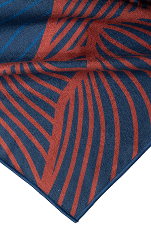 A close-up of a folded corner of a towel featuring a detailed abstract design. The towel is primarily dark blue with rust-red wavy lines that create a flowing, organic pattern. The fabric's texture is soft and smooth, with the stitching along the edge visible. The intricate lines and rich colors give the towel a bold and artistic appearance, emphasizing quality and craftsmanship.