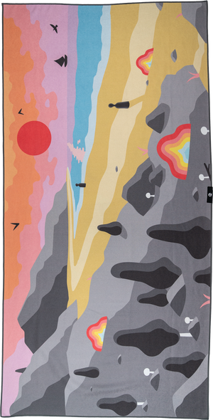 A towel with a dreamscape-inspired design featuring a surreal, colorful landscape. The left side has a gradient sky with pink, purple, and blue hues, dotted with abstract bird silhouettes and a red sun. The right side showcases a mountain range with jagged gray rocks, rock climbing holds, and bright lava-like patterns. A sandy yellow section separates the sky from the mountain, creating a playful and imaginative scene blending nature and fantasy.