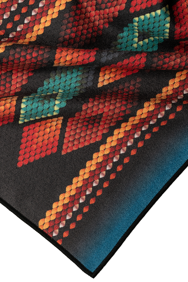 A close-up of a towel corner highlighting a vibrant diamond pattern with rich shades of red, orange, and teal on a black background. The intricate detailing and texture create a dynamic and eye-catching design, perfect for adding a bold accent to your outdoor adventures.