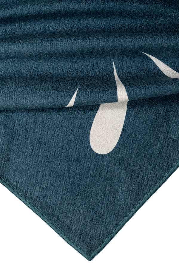 Close-up of the towel corner showing a smooth, dark teal fabric with a white water droplet design, highlighting the towel's soft texture and intricate edge stitching.