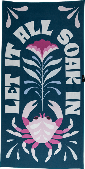 A playful towel with a pink crab, flower, and water droplets, framed by the bold text "LET IT ALL SOAK IN." The dark teal background and bright accents create a fun, vibrant beach vibe.