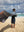 A man holds a towel from his shoulders as it blows in the Tradewinds on a Hawaiian beach