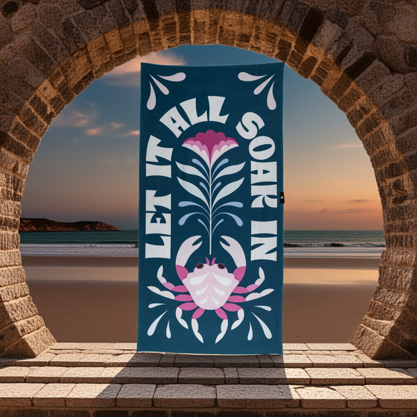 Decorative towel with floral and crab design in front of a stone archway with a beach view.