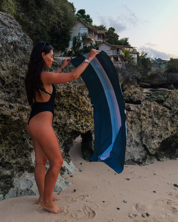 A woman spreading out a towel on a beach in front of coral and rocks