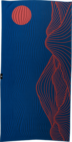 A blue towel featuring an abstract design with wavy, curved lines. The right side has red flowing lines resembling a mountainous or canyon-like shape, while the upper left corner displays a red circular shape with similar wavy lines, evoking the image of a setting sun. The overall design gives a sense of movement and natural elements, blending earthy and modern styles.