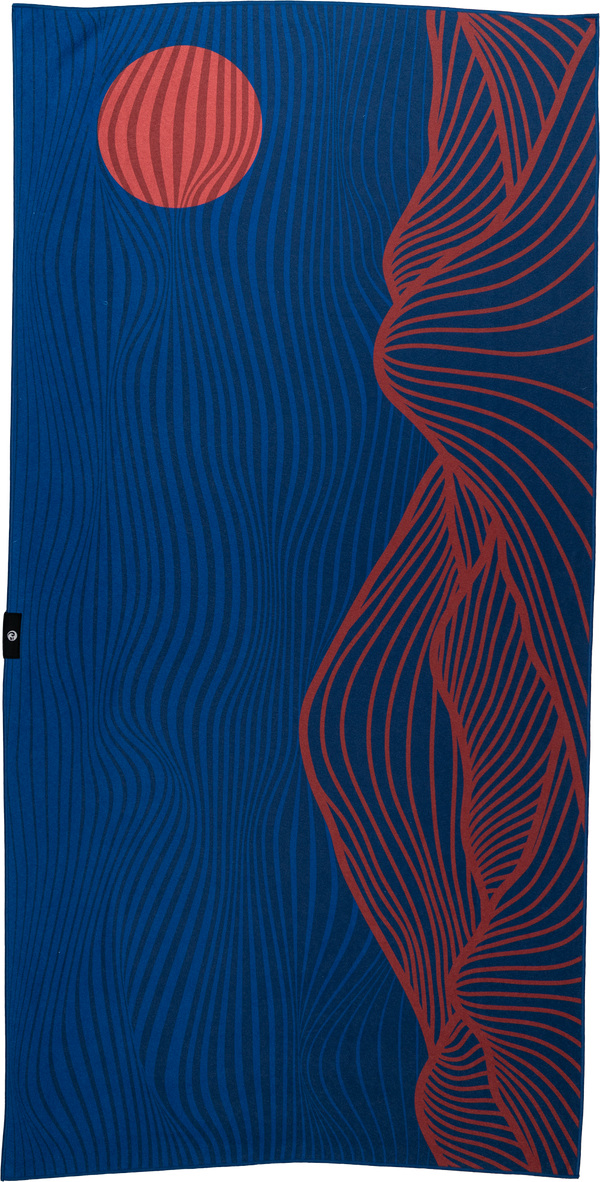 A blue towel featuring an abstract design with wavy, curved lines. The right side has red flowing lines resembling a mountainous or canyon-like shape, while the upper left corner displays a red circular shape with similar wavy lines, evoking the image of a setting sun. The overall design gives a sense of movement and natural elements, blending earthy and modern styles.