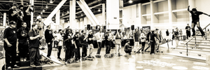 Black and white photo of a skateboarding event with people and skateboards in an indoor arena.