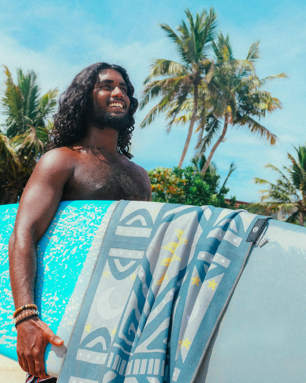 A happy faced towel draped over a surfboard. a man smiling looking out at the ocean