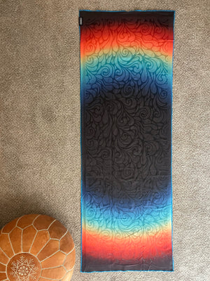Yoga mat with a colorful pattern on a beige carpet showing the silicone pattern for a Happy Faced Super Grip Towel