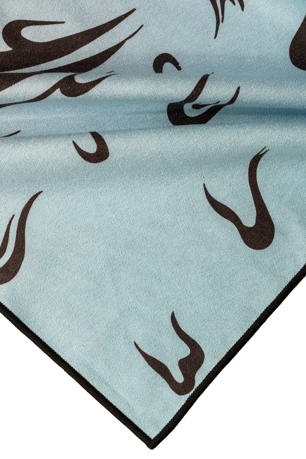 A close-up corner view of a towel featuring a light blue background with black abstract, flame-like shapes. The towel has a smooth texture and a dark edge lining that contrasts with the light background. The subtle yet dynamic design elements create a modern and minimal aesthetic, emphasizing the flowing shapes across the fabric. High Quality.