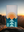 Towel with mountain and sun design held up against a mountainous landscape with sunset.