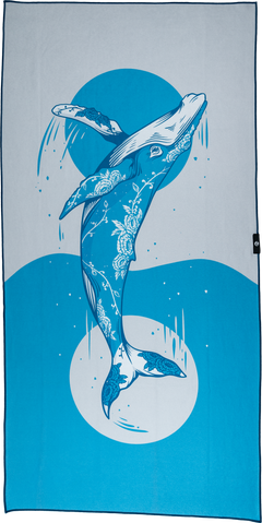 A beach towel featuring a blue and white whale design against a beach setting, with a large whale in the foreground and smaller whales in the background. for Happy Faced Towels