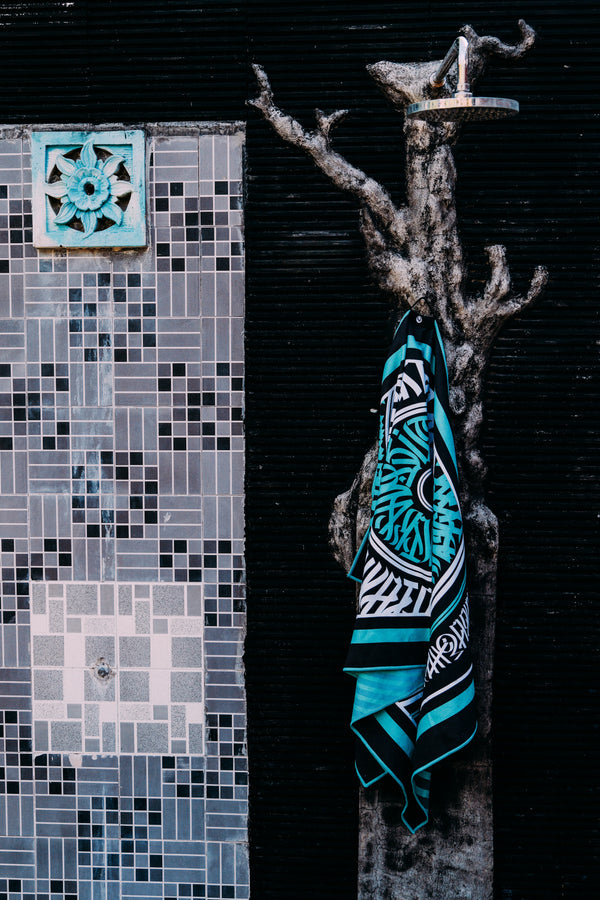 The Whats Good Towel from Happy Faced Towels hangs in an outdoor shower with patterned tile