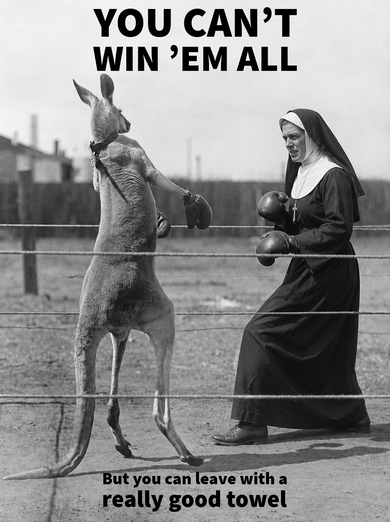 Black and white humorous poster featuring a kangaroo wearing boxing gloves facing a nun in boxing gloves inside a ring, with bold text reading 'YOU CAN'T WIN 'EM ALL' at the top and 'But you can leave with a really good towel' at the bottom. Happy Faced Towels