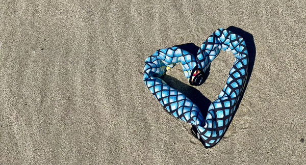 Blue and black patterned Happy Faced towel rolled up and shaped like a heart on a sandy beach