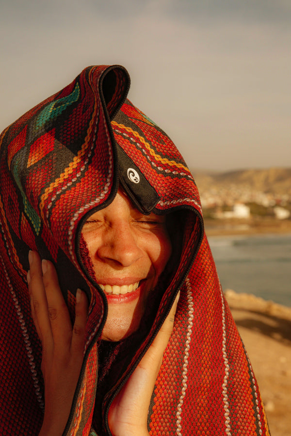 a woman with a Happy faced towel on her head smiling at the beach in Morocco.